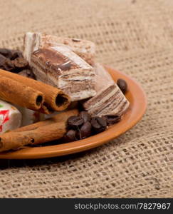 Sweets, cinnamon, nuts and coffee beans on a saucer, on burlap background.