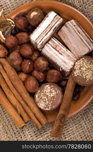 Sweets, cinnamon, nuts and coffee beans on a saucer, on burlap background.