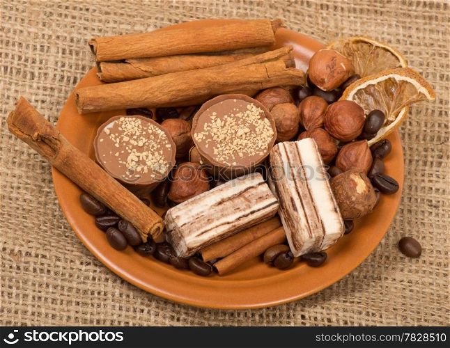 Sweets, cinnamon, nuts and coffee beans on a saucer, on burlap background.