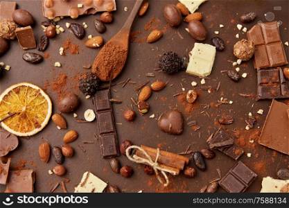 sweets, confectionery and culinary concept - cocoa beans, chocolate, nuts and cinnamon sticks on brown background. cocoa beans, chocolate, nuts and cinnamon sticks