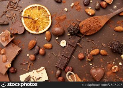 sweets, confectionery and culinary concept - cocoa beans, chocolate, nuts and cinnamon sticks on brown background. cocoa beans, chocolate, nuts and cinnamon sticks