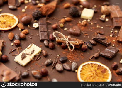 sweets, confectionery and culinary concept - cocoa beans, chocolate, nuts and cinnamon sticks on brown background. cocoa beans, chocolate, nuts and cinnamon sticks