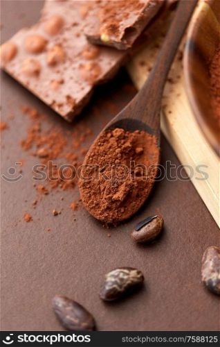 sweets, confectionery and culinary concept - cocoa powder in wooden spoon with chocolate and beans on brown background. cocoa powder on wooden spoon with chocolate