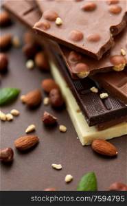 sweets, confectionery and food concept - bars of dark, white and milk chocolate with nuts on brown background. close up of different chocolate bars and nuts