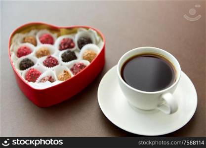 sweets, confectionery and food concept - candies in red heart shaped chocolate box and cup of coffee on brown background. candies in heart shaped chocolate box and coffee