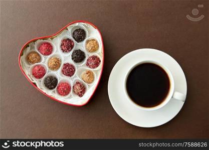 sweets, confectionery and food concept - candies in red heart shaped chocolate box and cup of coffee on brown background. candies in heart shaped chocolate box and coffee
