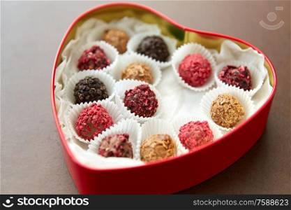 sweets, confectionery and food concept - candies in red heart shaped chocolate box on brown background. candies in red heart shaped chocolate box