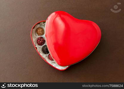 sweets, confectionery and food concept - candies in red heart shaped chocolate box on brown background. candies in red heart shaped chocolate box