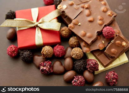 sweets, confectionery and food concept - close up of different chocolate bars, candies and gift box on brown background. close up of different chocolates, candies and gift