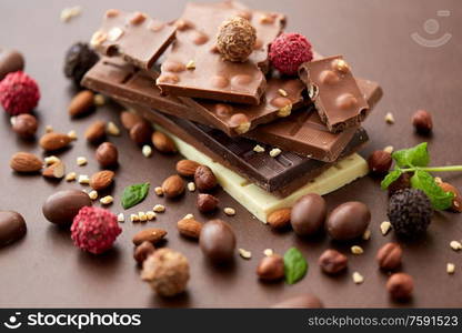 sweets, confectionery and food concept - close up of different chocolate bars, candies and nuts on brown background. close up of different chocolates, candies and nuts