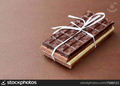 sweets, confectionery and food concept - different kinds of chocolate tied with white ribbon on brown background. different kinds of chocolate on brown background