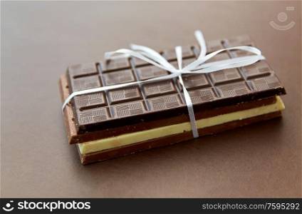 sweets, confectionery and food concept - different kinds of chocolate tied with white ribbon on brown background. different kinds of chocolate on brown background