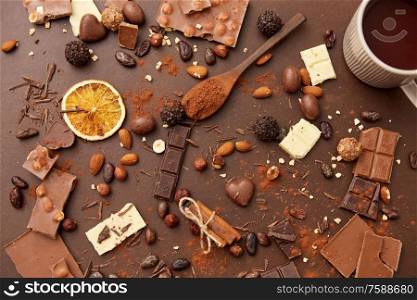 sweets, confectionery and food concept - hot chocolate with nuts, candies, cinnamon and cocoa powder on brown background. hot chocolate with nuts, cocoa powder and candies