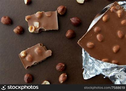 sweets, confectionery and food concept - milk chocolate bar with hazelnuts in foil wrapper on brown background. milk chocolate bar with hazelnuts in foil wrapper