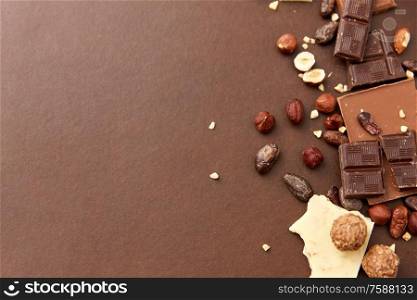 sweets, confectionery and food concept - milk, dark and white chocolate bars with hazelnuts and cocoa beans on brown background. chocolate bars with hazelnuts and cocoa beans