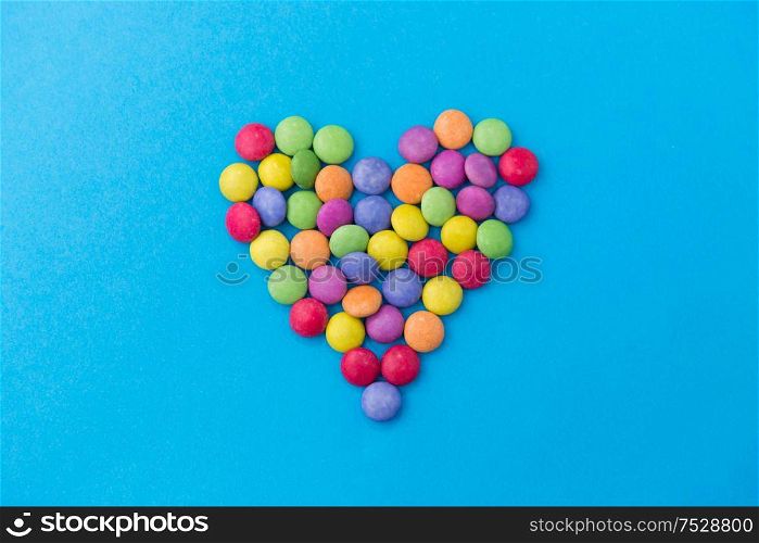 sweets, confectionery and valentine&rsquo;s day concept - bright multicolored candy drops in shape of heart on blue background. candy drops in shape of heart on blue background