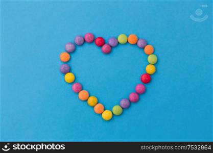 sweets, confectionery and valentine&rsquo;s day concept - bright multicolored candy drops in shape of heart on blue background. candy drops in shape of heart on blue background