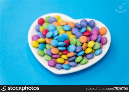 sweets, confectionery and valentine&rsquo;s day concept - candy drops on heart shaped plate over blue background. candies on heart shaped plate over blue background