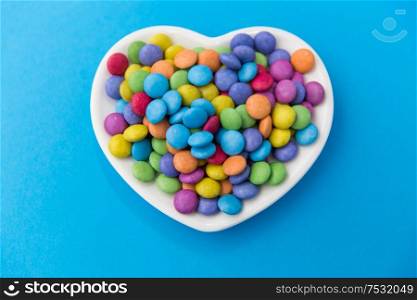 sweets, confectionery and valentine&rsquo;s day concept - candy drops on heart shaped plate over blue background. candies on heart shaped plate over blue background