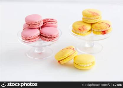 sweets, pastry and food concept - lemon yellow and pink macarons on glass confectionery stand over white background. macarons on glass confectionery stand