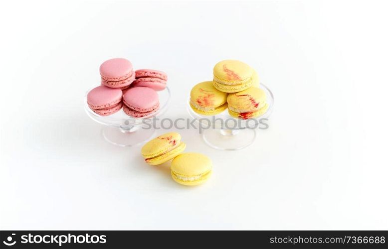 sweets, pastry and food concept - lemon yellow and pink macarons on glass confectionery stand over white background. macarons on glass confectionery stand