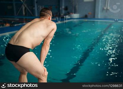 Swimmer in goggles prepares to jump into the water, back view. Workout in swimming pool, healthy activity