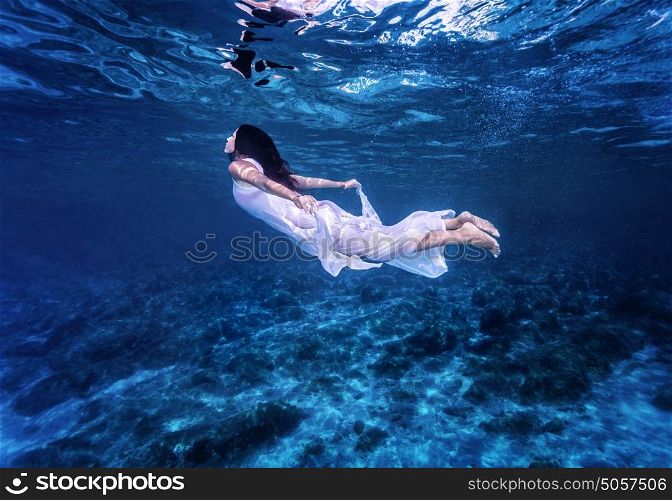 Swimming in beautiful blue sea, gentle woman in white fashion dress diving underwater, refreshment and enjoyment concept
