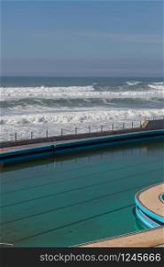 Swimming pool on ocean coast, moviment waves with foam. Wind power. Turquoise water.