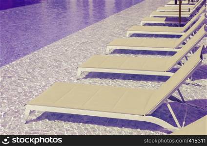 Swimming pool with clean water and sunbeds in purple and yellow tone color