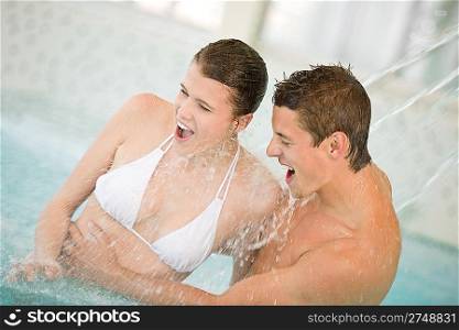 Swimming pool - young couple have fun under water stream on honeymoon