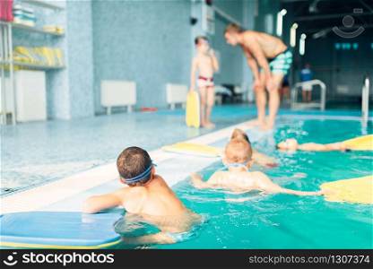 Swimming sports activity. Children swimming in pool. Healthy and happy childhood concept. Kids in water with planks for swimming. Instructor talking to child on background.. Children swimming in pool