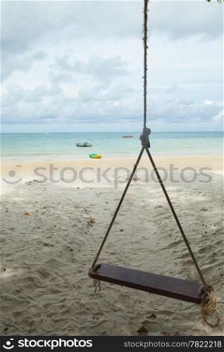 Swing on the beach with a boat parked under a tree close to the sea.