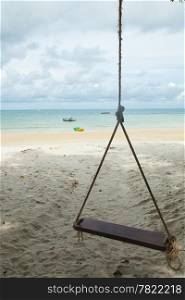 Swing on the beach with a boat parked under a tree close to the sea.