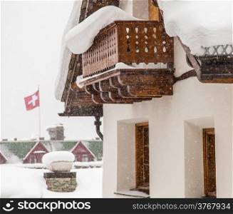 Swiss chalet during heavy snow with Swiss flag in background