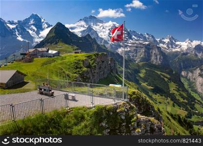 Swiss flag waving and tourists admire the peaks of Monch and Jungfrau mountains on a Mannlichen viewpoint, Bernese Oberland Switzerland. Mannlichen viewpoin, Switzerland