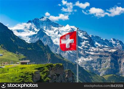 Swiss flag waving and tourists admire the peaks of Monch and Jungfrau mountains on a Mannlichen viewpoint, Bernese Oberland Switzerland. Mannlichen viewpoint, Switzerland