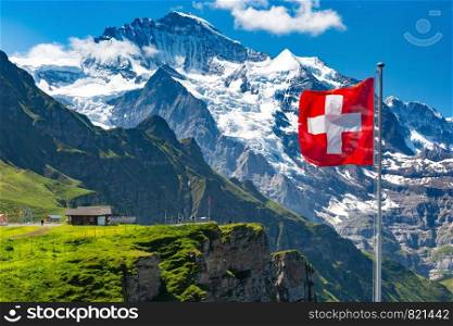 Swiss flag wavingon a Mannlichen viewpoint with peak of Jungfrau mountain on the background, Bernese Oberland Switzerland. Mannlichen viewpoin, Switzerland