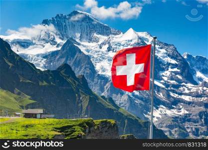 Swiss flag wavingon a Mannlichen viewpoint with peak of Jungfrau mountain on the background, Bernese Oberland Switzerland. Mannlichen viewpoint, Switzerland