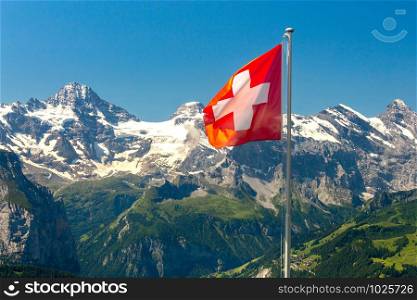 Swiss national flag on a background of snow-capped mountains. Mannlichen.. View of the Swiss Alps near the city of Lauterbrunnen. Switzerland.