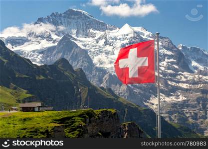 Swiss national flag on a background of snow-capped mountains. Mannlichen.. View of the Swiss Alps near the city of Lauterbrunnen. Switzerland.