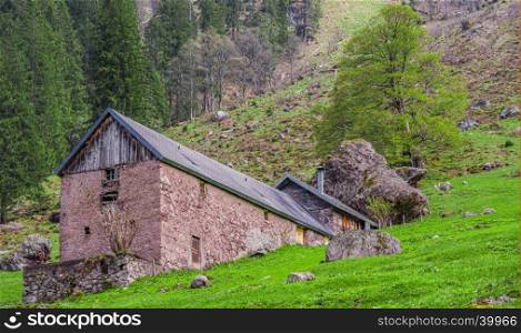 Swiss traditional stable and house built with stone wall and shingle roof, enclosed by a huge fallen mountain rock.