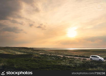Sylt island landscape with a car on a road going through green moss dunes at the golden hour of the morning, on a sunny day, in Germany.