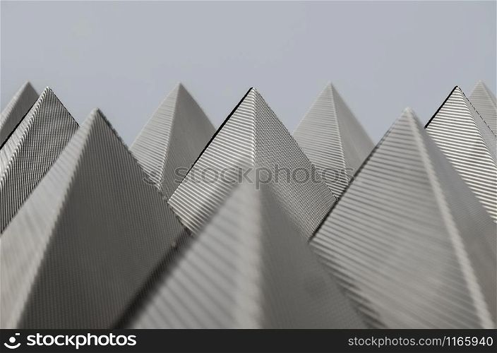 Symmetric piramidal pattern made of metallic planes with little holes in the Navarrabiomed building in Pamplona, Navarra, Spain. Symmetric, metallic, piramid pattern over grey sky in the Navarr