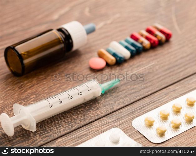 Syringe, capsules, pills and medical bottle lie diagonally on a wooden table.. Syringe and capsule, medical ampoule and tablets on a wooden table.