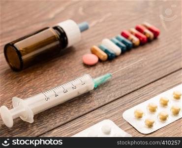 Syringe, capsules, pills and medical bottle lie diagonally on a wooden table.. Syringe and capsule, medical ampoule and tablets on a wooden table.