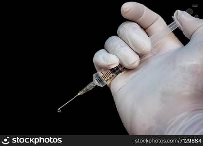 Syringe in a hand in medical gloves, ready for injection with medication. Black background