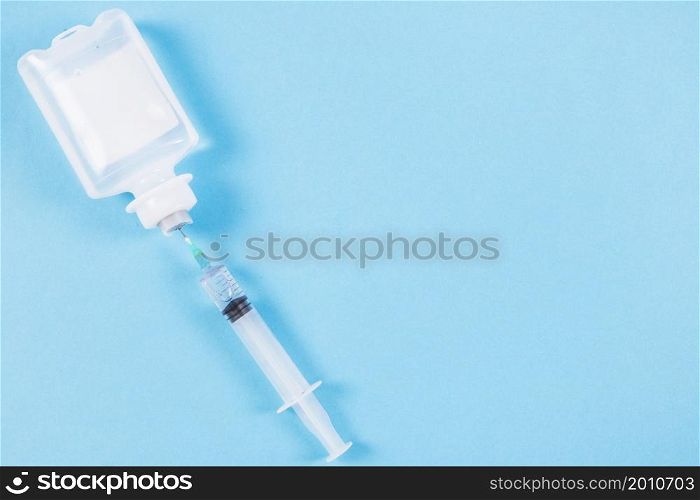 syringe inserted normal saline solution plastic bottle blue background
