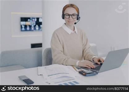 System administrator at workplace in office. Young woman is consultant of call center. European friendly girl in headset is talking to client. Customer support concept.. System administrator at workplace. Young woman in headset is consultant of call center.