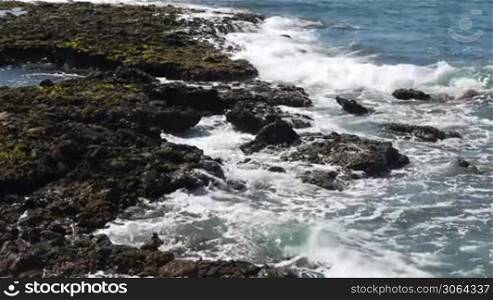 Szene zeigt einen steinigen Strand mit starken Wellen. Scene shows a rocky beach with strong waves.