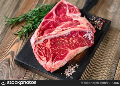 T-bone steak with seasonings on the wooden board: top view